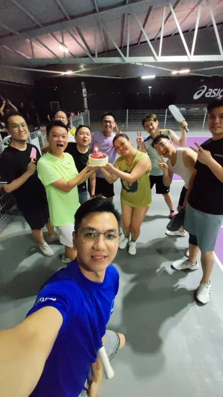 球场上十来个人围着一个插着蜡烛的蛋糕合照